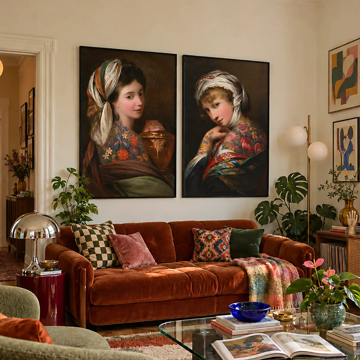 A styled living room featuring two large framed classical-style portrait paintings on the wall above a rust-brown velvet sofa with patterned pillows and a throw blanket.