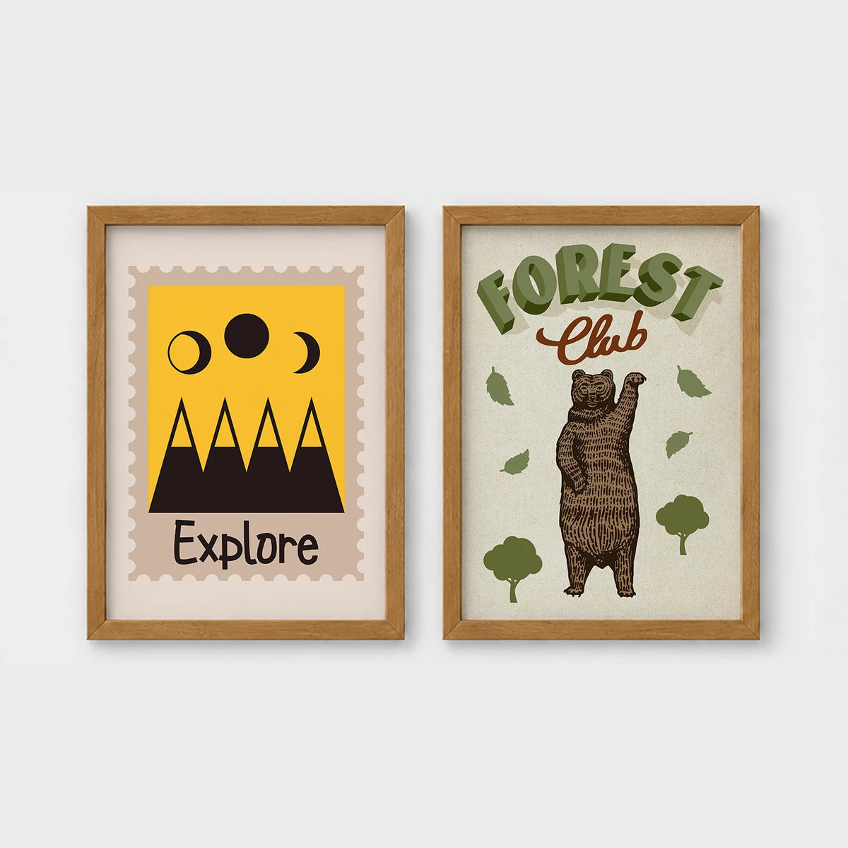 Set of 2 framed prints, stamp-style and illustrated kids prints: an "Explore" stamp-style icon illustration of mountains and moon phases; and a "Forest Club" illustration of a bear among trees — unframed