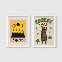 Set of 2 framed prints, stamp-style and illustrated kids prints: an "Explore" stamp-style icon illustration of mountains and moon phases; and a "Forest Club" illustration of a bear among trees — unframed