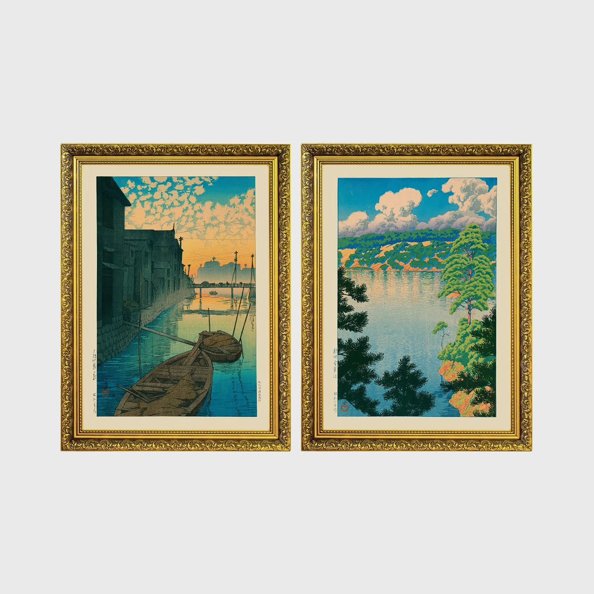 Set of 2 framed prints, Kawase Hasui Japanese woodblock prints: boats moored on a canal at dawn beneath a cloud-streaked sky; and a lake view framed by pine branches beneath drifting clouds — unframed