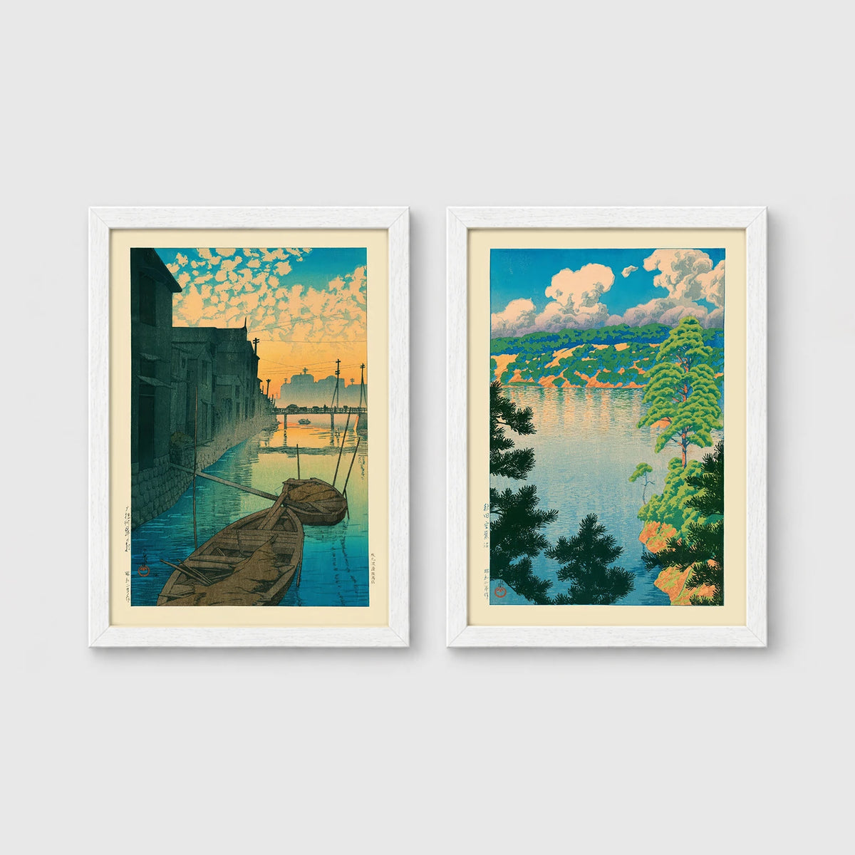 Set of 2 framed prints, Kawase Hasui Japanese woodblock prints: boats moored on a canal at dawn beneath a cloud-streaked sky; and a lake view framed by pine branches beneath drifting clouds — unframed