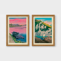 Set of 2 framed prints, Kawase Hasui Japanese woodblock prints: a pink sunset lake scene with a moored boat; and green coastal cliffs with a small sailboat — unframed
