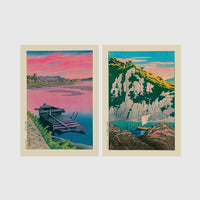 Set of 2 framed prints, Kawase Hasui Japanese woodblock prints: a pink sunset lake scene with a moored boat; and green coastal cliffs with a small sailboat — unframed