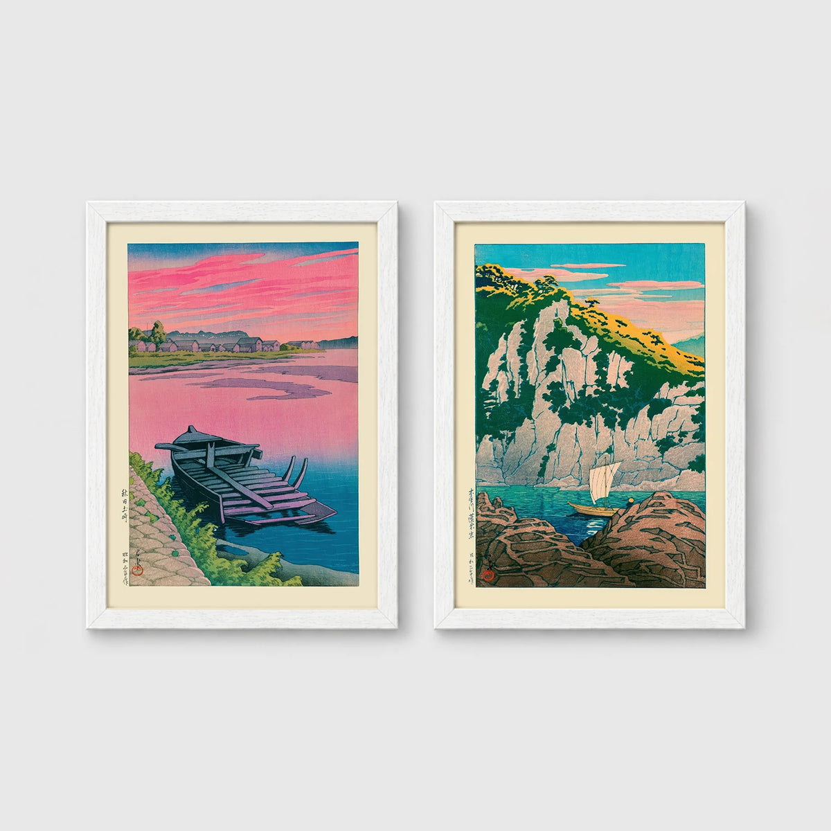 Set of 2 framed prints, Kawase Hasui Japanese woodblock prints: a pink sunset lake scene with a moored boat; and green coastal cliffs with a small sailboat — unframed