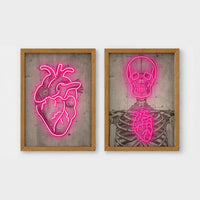 Set of 2 framed prints, neon anatomical illustrations: a neon pink anatomical heart illustration; and a neon pink skeleton skull and ribcage illustration — unframed