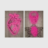 Set of 2 framed prints, neon anatomical illustrations: a neon pink anatomical heart illustration; and a neon pink skeleton skull and ribcage illustration — unframed