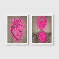 Set of 2 framed prints, neon anatomical illustrations: a neon pink anatomical heart illustration; and a neon pink skeleton skull and ribcage illustration — unframed
