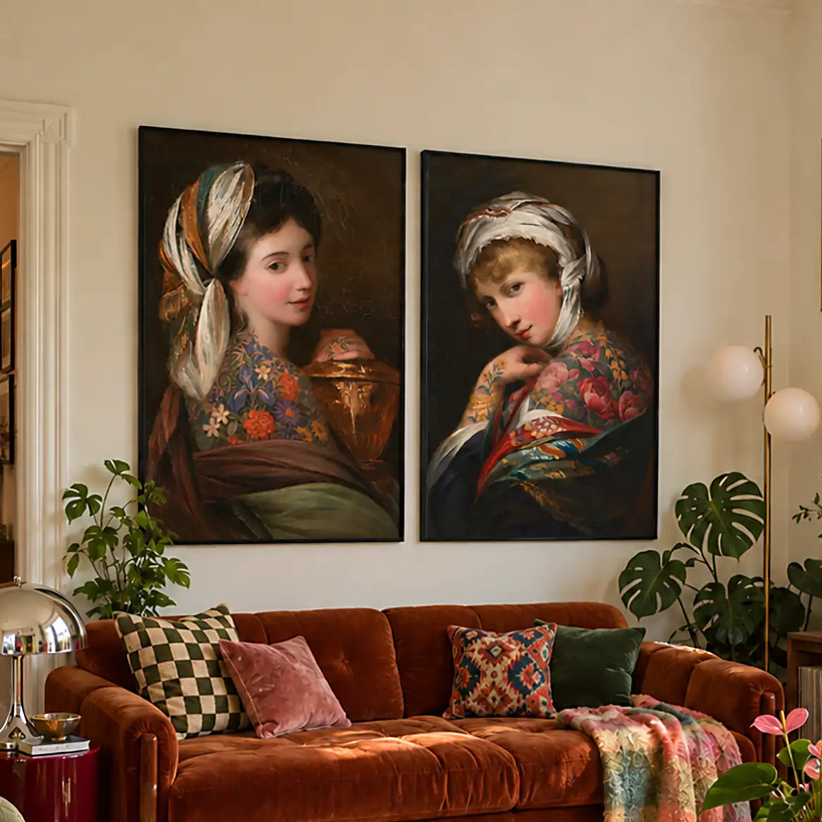 A styled living room featuring two large framed classical-style portrait paintings on the wall above a rust-brown velvet sofa with patterned pillows and a throw blanket.