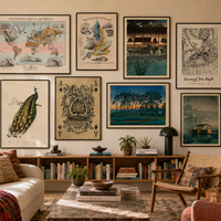 A styled living room featuring a gallery wall of eight framed vintage-style prints and posters, including maps, a peacock illustration, playing cards, and landscape scenes, above a bookshelf and sofa.