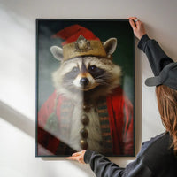 Framed Christmas raccoon portrait print in a red costume and gold hat, held against a white wall.