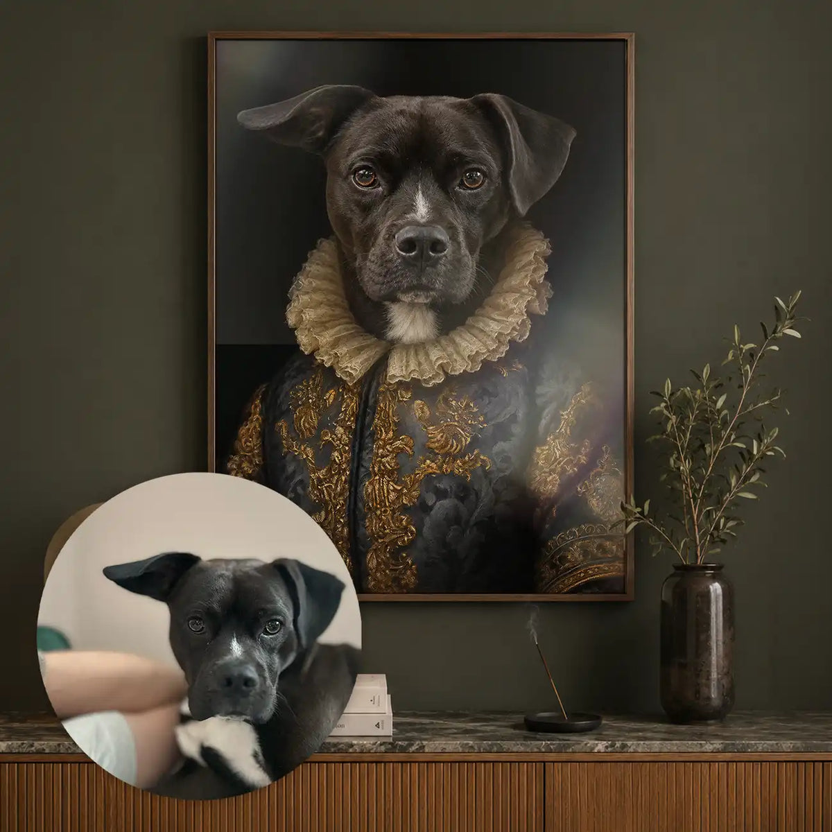 A framed custom pet portrait of a black dog dressed in a gold-embroidered historical coat with a ruffled collar, displayed on a dark wall above a wooden console. A circular inset shows the original reference photo of the dog used for the portrait.
