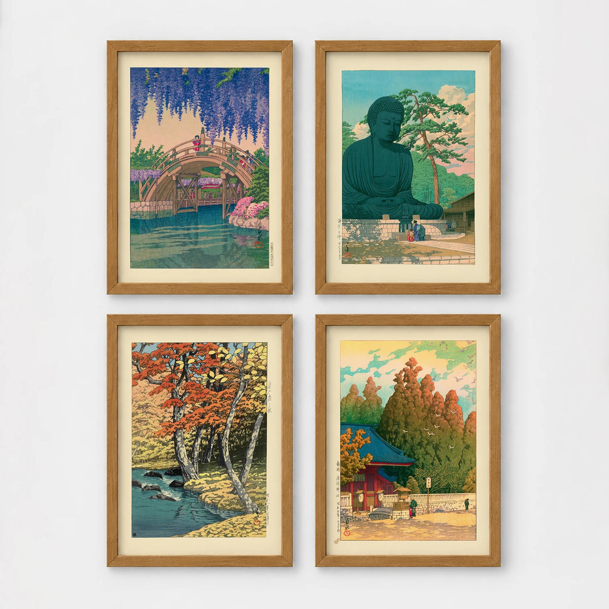 Set of 4 framed prints, Kawase Hasui Japanese woodblock prints (landmarks): a red arched bridge beneath cascading wisteria and cherry blossom; the Great Buddha of Kamakura among pine trees; a stream through autumn foliage; and a red pagoda gate in an autumn forest — unframed