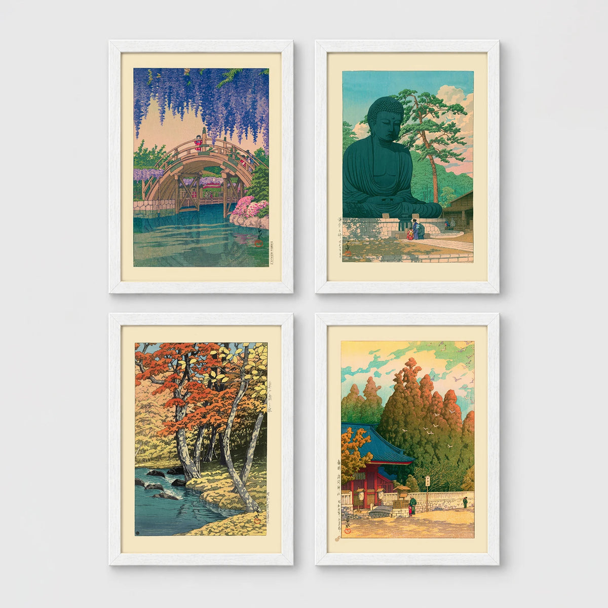 Set of 4 framed prints, Kawase Hasui Japanese woodblock prints (landmarks): a red arched bridge beneath cascading wisteria and cherry blossom; the Great Buddha of Kamakura among pine trees; a stream through autumn foliage; and a red pagoda gate in an autumn forest — unframed