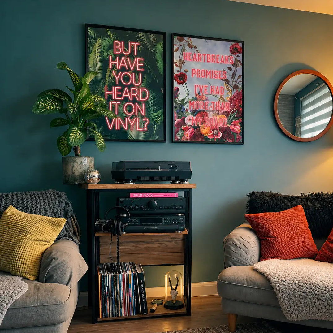 A styled living room corner with a teal wall, two framed floral and text posters, a plant, a record player, and two upholstered armchairs with orange and yellow pillows.