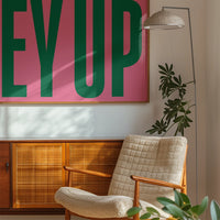 The print Ey Up styled in a bedroom, bold green lettering on pink