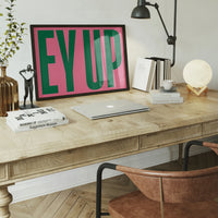 Ey Up print hanging in a dining room, large green capital letters on pink