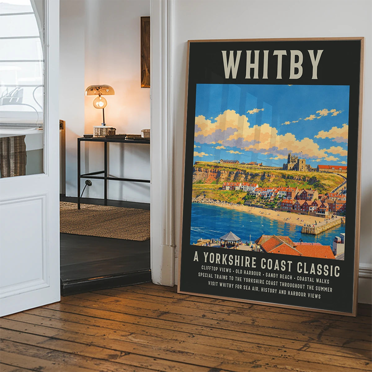 Whitby harbour poster art hanging in a hallway, with red-roofed cottages and blue sea
